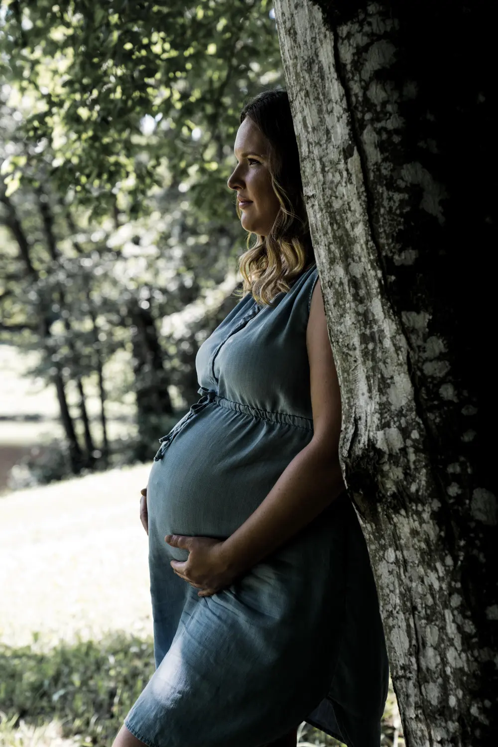 Melissa Herkommer Photography, Babybauch, eine schwangere Frau lehnt sich an einen Baum