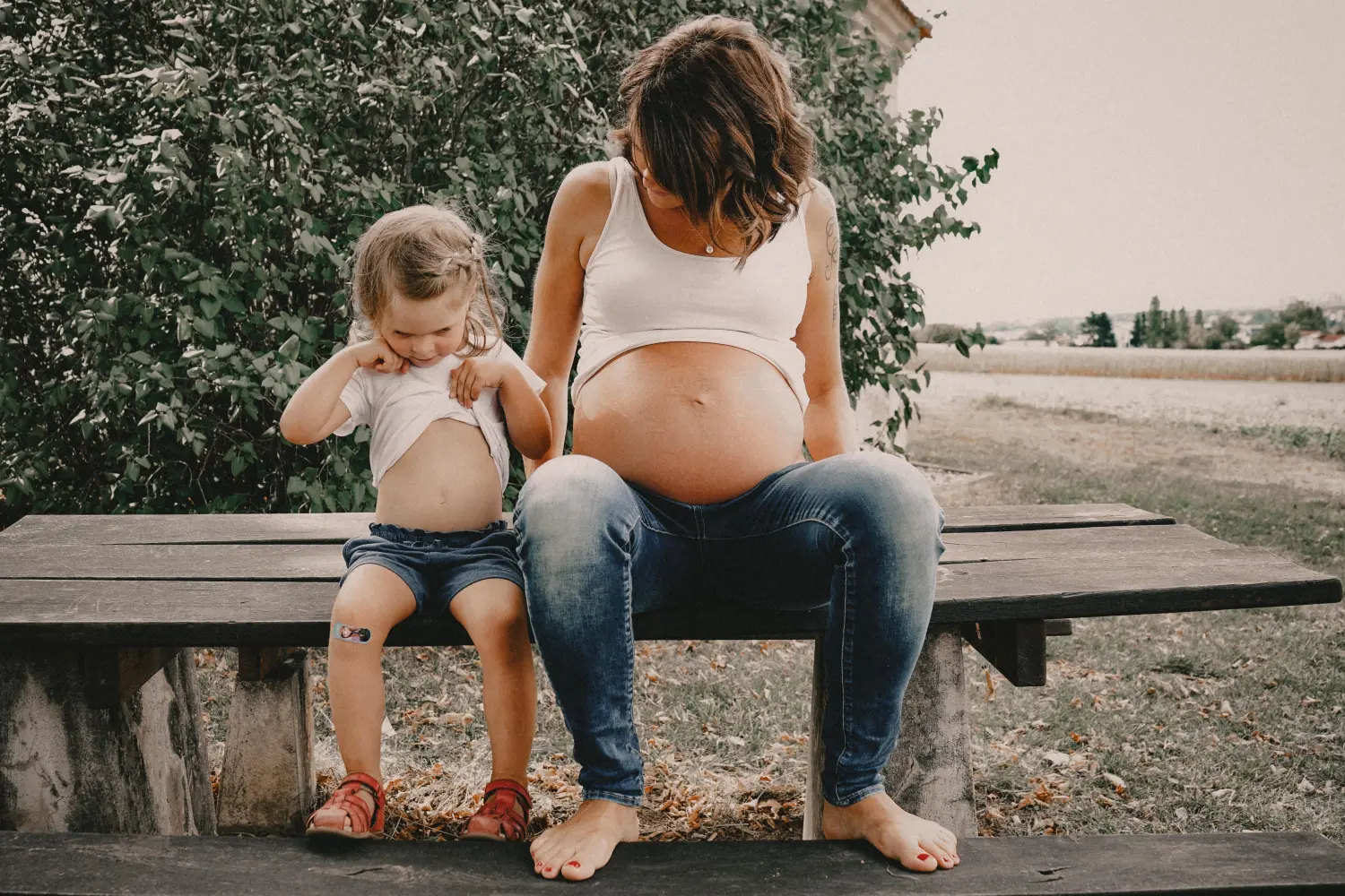 Melissa Herkommer Photography, Babybauch, Mama und Kind sitzen auf der Bank und zeigen ihren Bauch